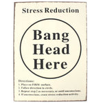 A rectangular tin sign with a cream coloured front, black text, displaying the phrase 'Stress Reduction Bang Head Here' with directional instructions.