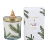 A Gisela Graham Cypress Pine scented candle in glass jar with green pine branch illustrations, featuring a gold lid with gold Christmas tree topper, shown next to its white gift box packaging, decorated with pine branches.